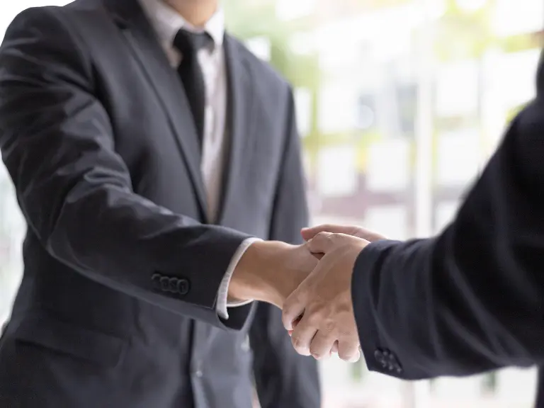 Aperto de mãos profissional entre dois homens de terno em ambiente de escritório.